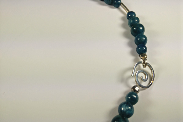 Apatit-Kette aus tief petrolfarbenen Steinen. Die mit Silberröchen kombinierten Perlen irisieren durch Lichteinfall mit dem sogenannten Katzenaugeneffekt. Der Schmuckverschluss kann vorne getragen werden